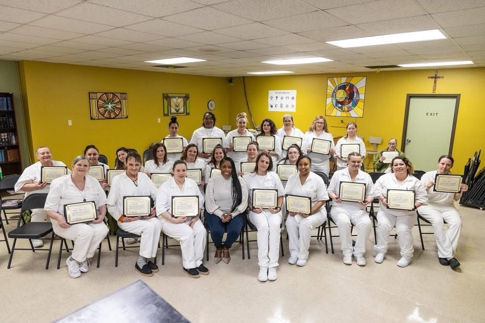 Program graduates in white holding their framed certificates at a completion ceremony